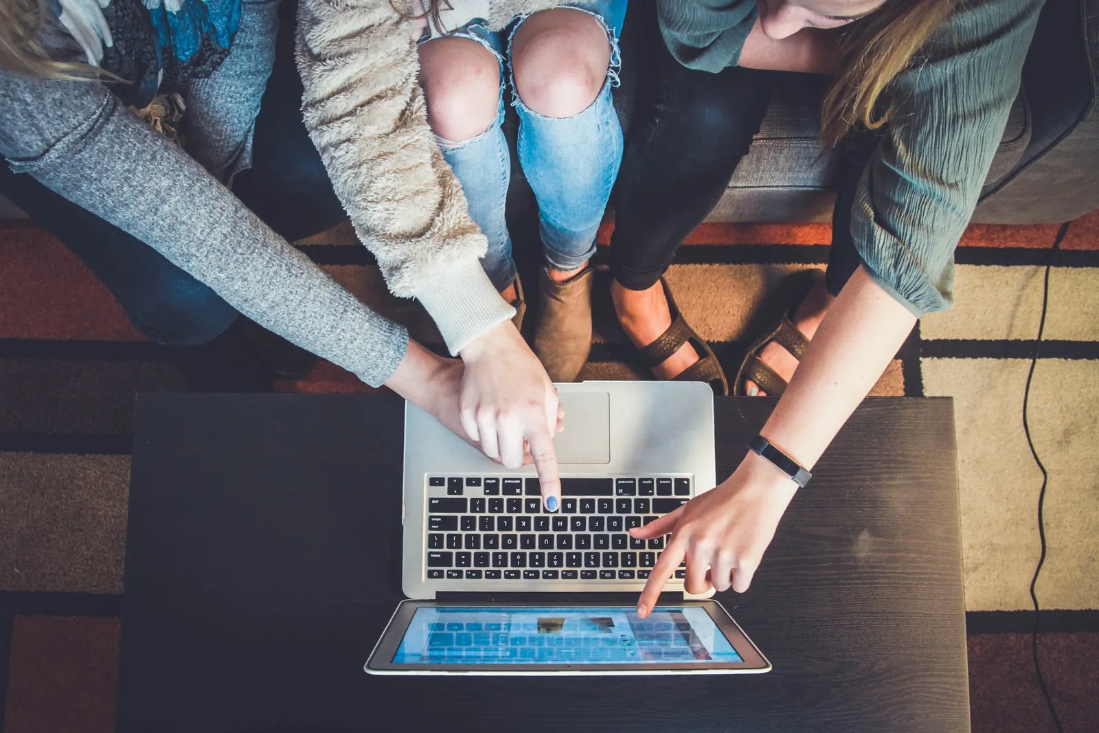 three people pointing the silver laptop computer